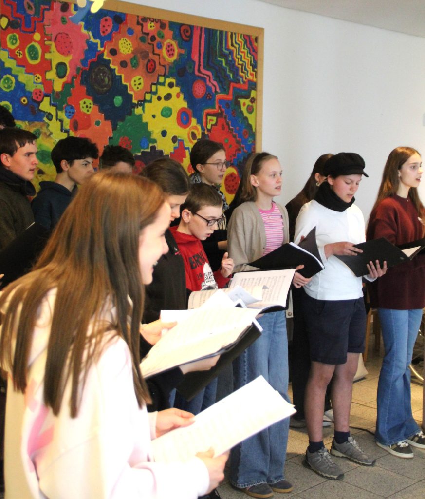 BLOG-Beitrag
FES-Schüler überraschen Bewohner im Altenzentrum musikalisch
Tränen der Rührung, Glück und Freude: So viele gute Gefühle in einem Gesicht ablesen zu können, ist wohl der beste Beweis für eine gelungene Aktion.
20 Schülerinnen und Schüler unseres FES-Jugendchors blickten bei ihrem kleinen musikalischen Ständchen im Eugen-Lederer-Altenzentrum in HDH am Mittwoch in ganz viele glückliche Gesichter: Die Schüler unseres FES-Gymnasiums und unserer FES-Realschule besuchten mit FES-Chorleiter Daniel Kindsvater und Schulleiter Andreas Borkeloh die Senioren im AWO-Altenzentrum in der Stadtmitte und überraschten mit europäischer Chormusik unterschiedlicher Stilistik aus dem aktuellen Konzertprogramm. Die Cafeteria war beim Besuch der jungen Sänger aus den Klassenstufen 7-10 proppenvoll gefüllt und die jungen Choristen erfüllten das Auditorium mit fröhlicher Musik. Besondere Freude bereitete den älteren Menschen, dass zum Abschluss des musikalischen Ständchens gemeinsam gesungen wurde. „Vielen Dank, dass Ihr heute bei uns seid. Unsere Bewohner freuen sich riesig, dass ihr für sie singt“, bedankte sich Nadine Schnell, Pflegedienstleitung im AWO-Altenzentrum am Ende des gut 30-minütigen kleinen chorischen Vortragsprogramms.
